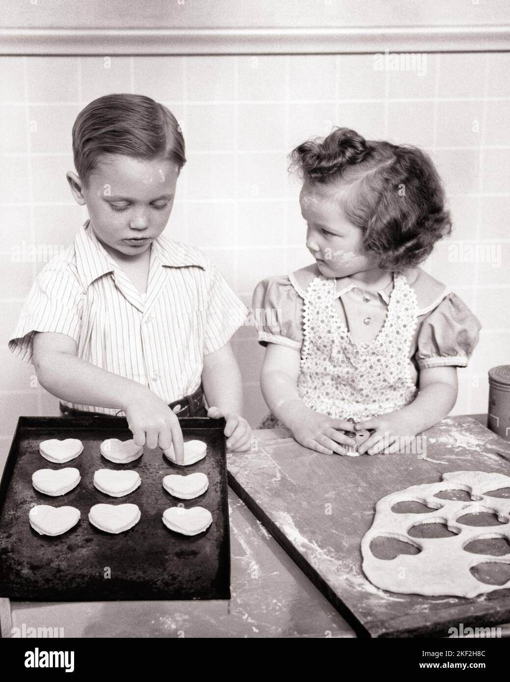 1940s HUMOR BOY AND GIRL IN KITCHEN MAKING HEART-SHAPED VALENTINE COOKIES BOY FOCUSED ON COOKIES GIRL FOCUSED ON BOY - v15 HAR001 HARS STRONG JOY LIFESTYLE SATISFACTION FEMALES STUDIO SHOT HOME LIFE COPY SPACE FRIENDSHIP HALF-LENGTH PERSONS THOUGHTFUL INSPIRATION CARING MALES COOKIES VALENTINES SAINT B&W GOALS HAPPINESS HIGH ANGLE VALENTINE'S TO RELATIONSHIPS CONNECTION CONCEPTUAL FEBRUARY FRIENDLY ST. SINCERE PERSONAL ATTACHMENT SYMBOLIC AFFECTION COOPERATION CREATIVITY EMOTION FOCUSED GROWTH INTENSE JUVENILES TOGETHERNESS VALENTINES DAY BLACK AND WHITE CAREFUL CAUCASIAN ETHNICITY EARNEST Stock Photo
