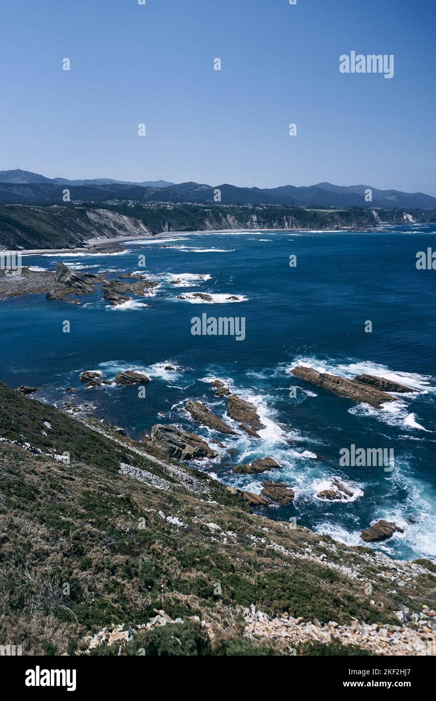landscape of the impressive cliffs and rocks of the Cantabrian sea coast with violent waves on a clear day next to the mountains, asturias, spain Stock Photo