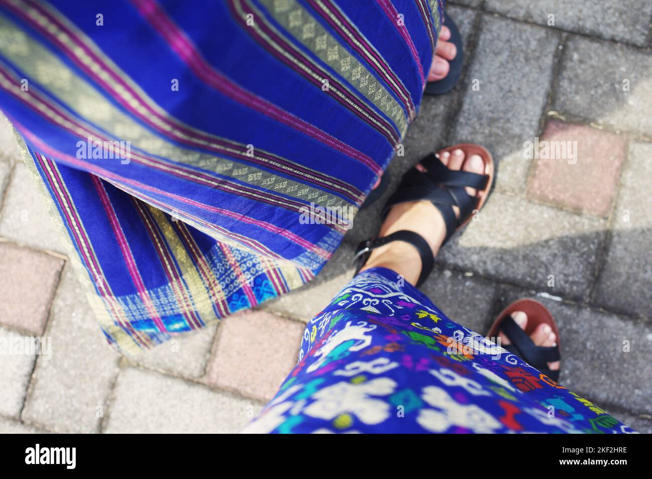 Two tourists in sandals wearing blue embroidered and batik patterned sarongs at a temple in Ubud — Bali, Indonesia Stock Photo