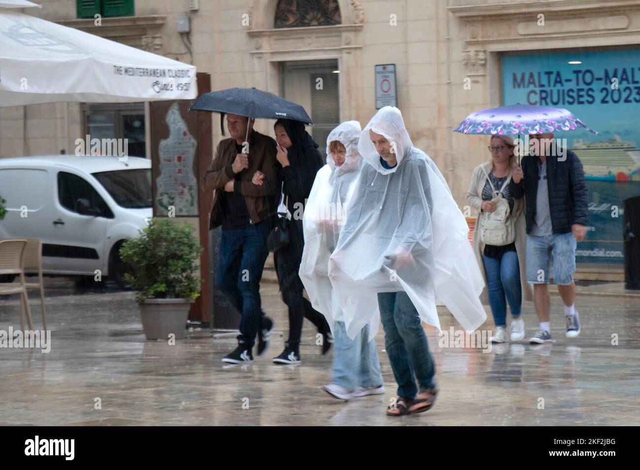 Valletta, Malta - November 12, 2022: People wearing rain ponchos and holding umbrellas walking on a rainy day Stock Photo