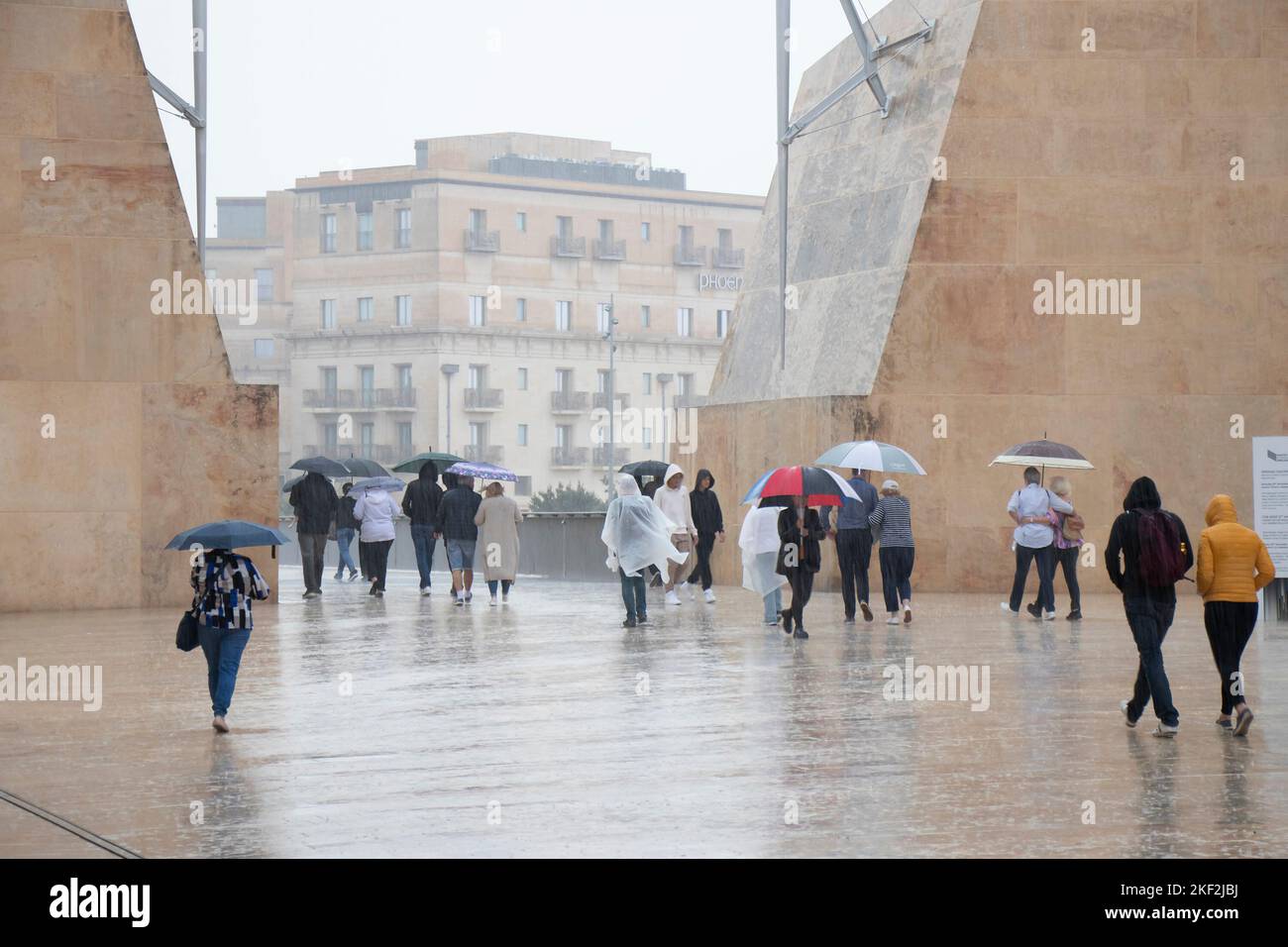 Valletta, Malta - November 12, 2022: People wearing rain ponchos and holding umbrellas walking on a rainy day Stock Photo