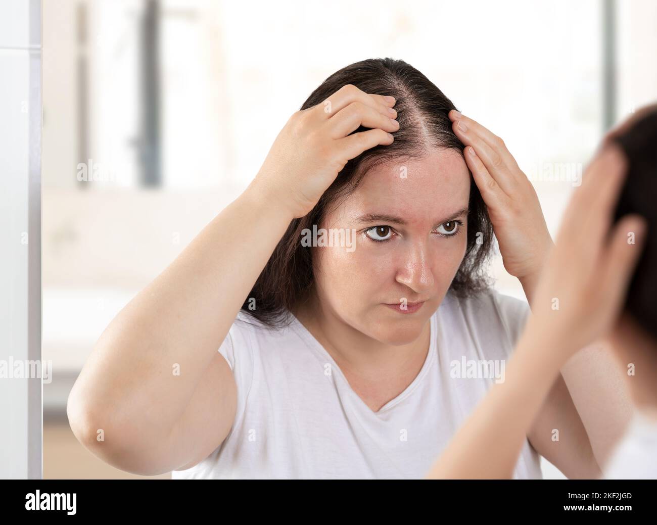 Woman controls hair loss and unhappy gazing at you in the mirror Stock Photo