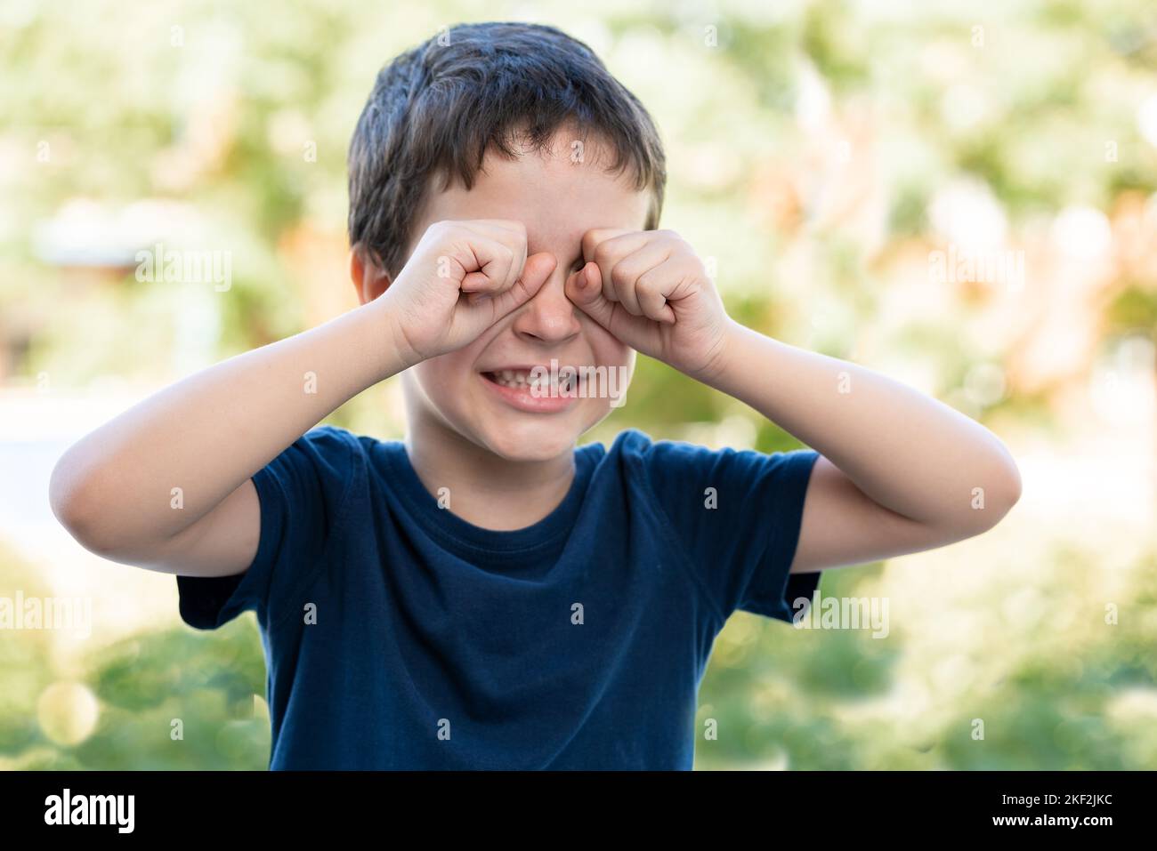 Child suffering itching scratching eyes outdoors in a park Stock Photo