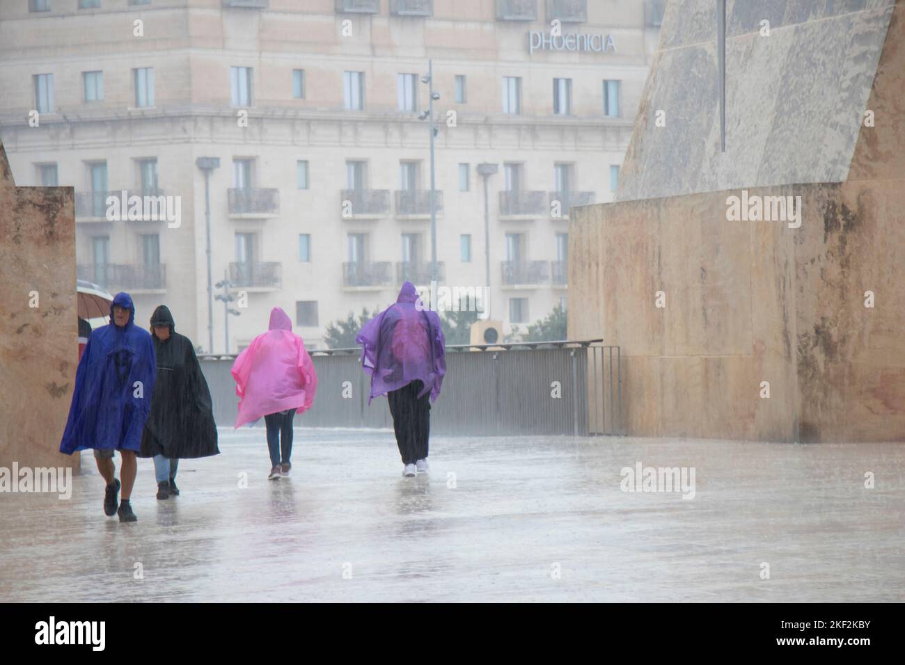 Valletta, Malta - November 12, 2022: People wearing rain ponchos and umbrellas walking on a rainy day Stock Photo