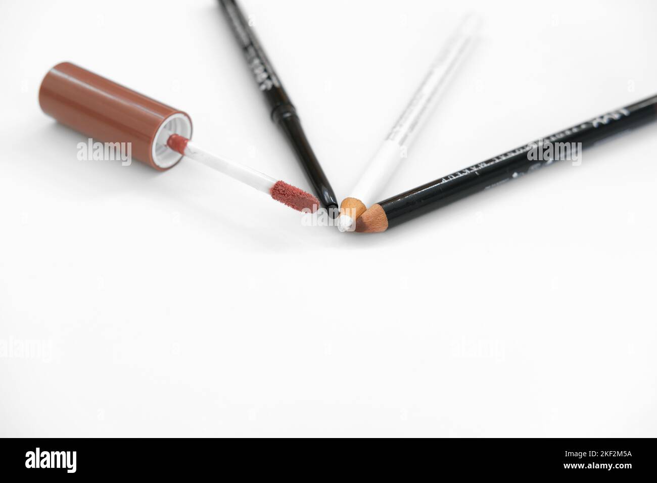 Lip gloss brush, brown lip pencil, black eye pencil and white eyeliner pencil on a white background; lips and eye makeup and cosmetics. Stock Photo