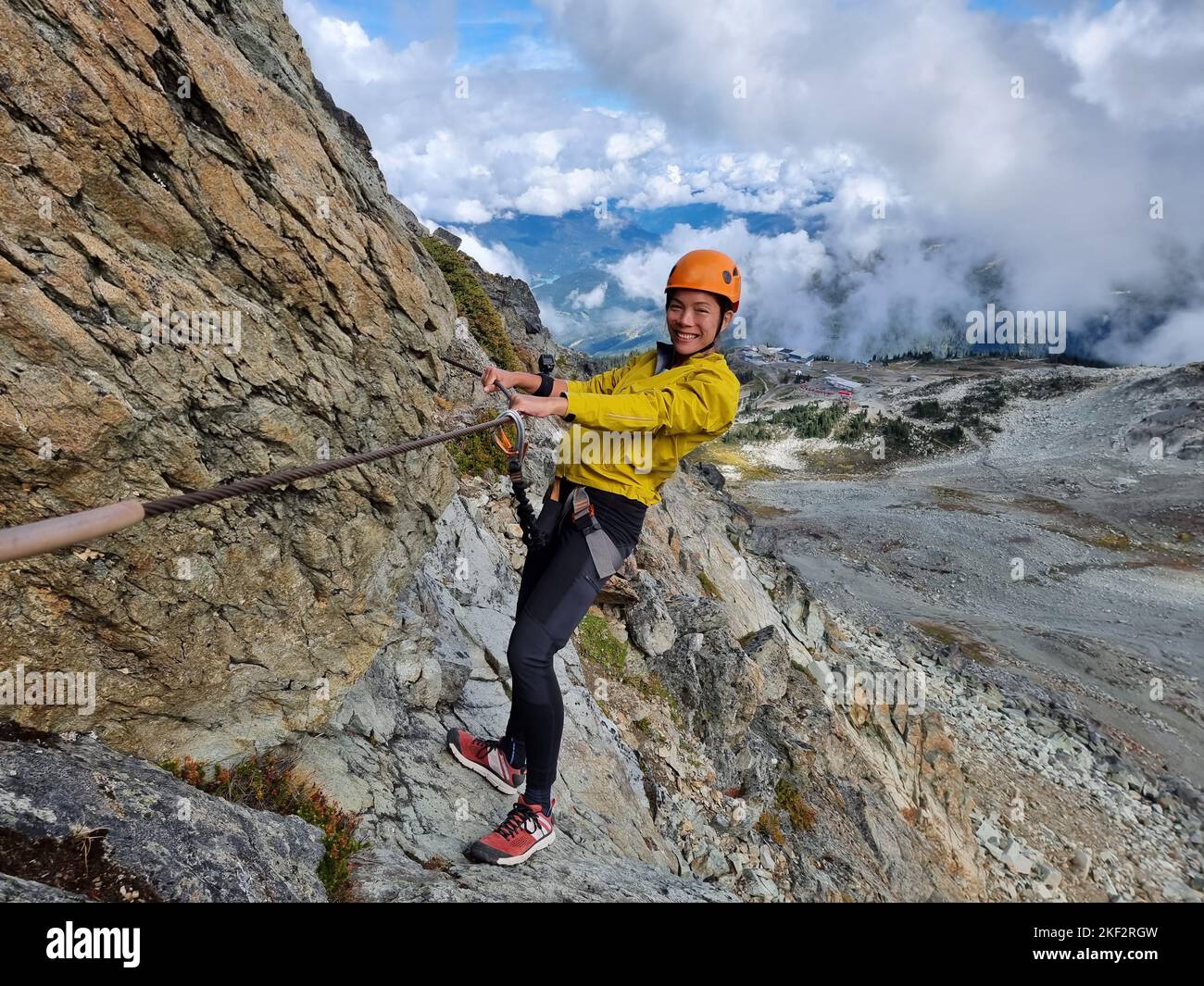 Via Ferrata climbing guided tour excursion happy Asian woman tourist hanging from rope at high pass on mountain side on Whistler peak, BC, Canada Stock Photo