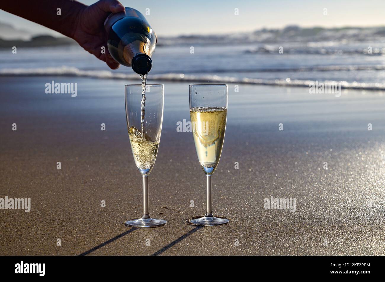 Pouring of cava or champagne sparkling white wine on white sandy ocean