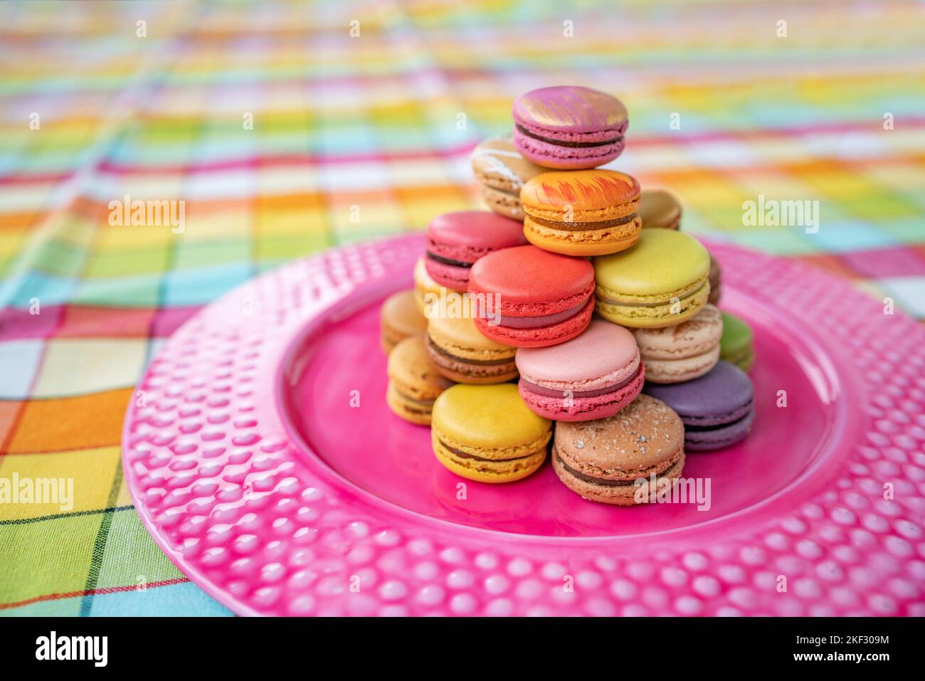 French pastry macarons tower presentation on pink dessert plate at bakery. Retro vintage checkered tablecloth table decor home kitchen. Assortment of Stock Photo