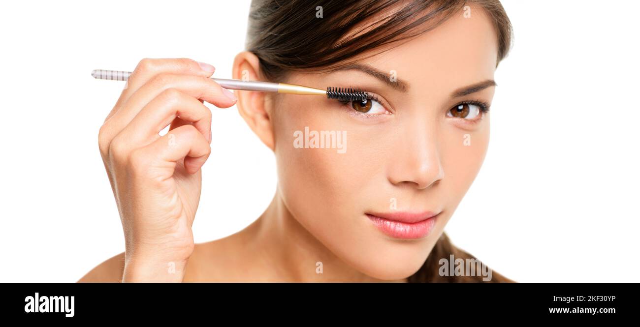 Mascara woman putting makeup on eyes. Asian female model face closeup with eye brush on eyelashes. Portrait isolated on white background Stock Photo