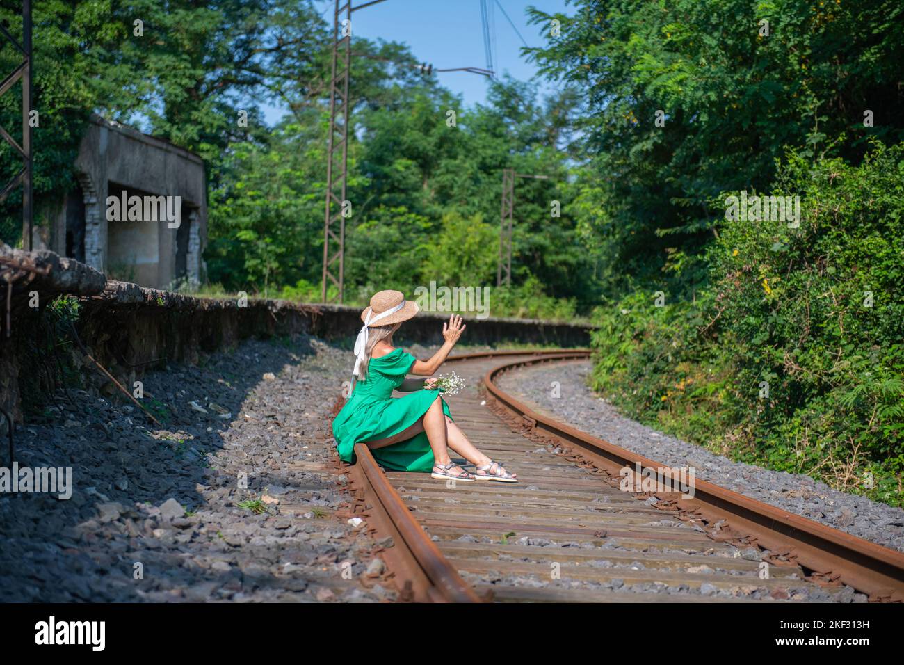 a young woman in a green dress is sitting on the railway Stock Photo ...
