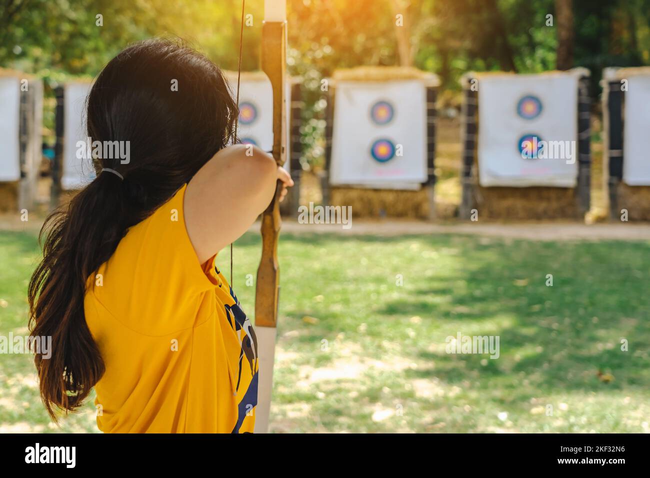 Back view of Asian girl wear eyeglasses with face mask aims archery bow and arrow to colorful