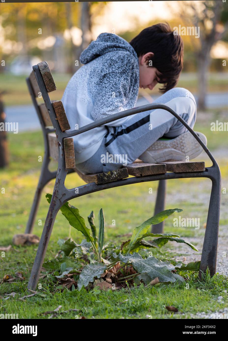 Boy curled up on a park bench doing something with focused attention