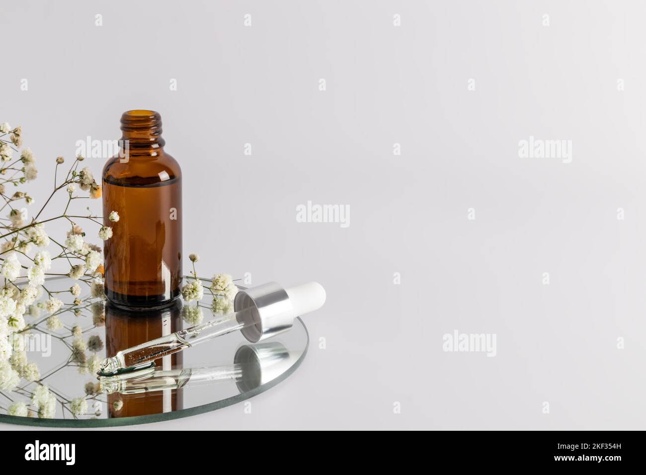 an open bottle with a moisturizer and skin nourishing agent stands on a round mirror with a filled pipette. a copy of the space. selective focus Stock Photo