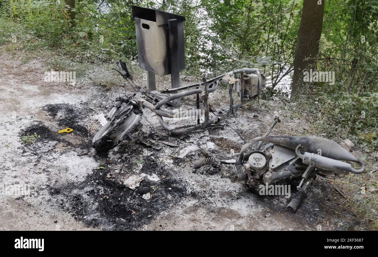 A burnt motorcycle lying on the ground next to a trash can Stock Photo