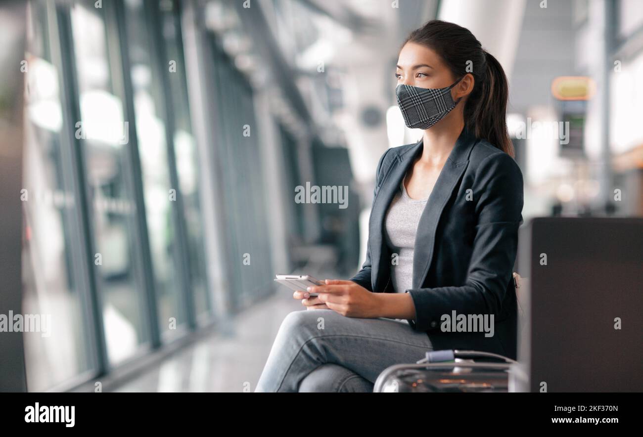 Travel during coronavirus. Asian business woman wearing face mask in airport terminal waiting for flight thinking looking out the window using phone Stock Photo