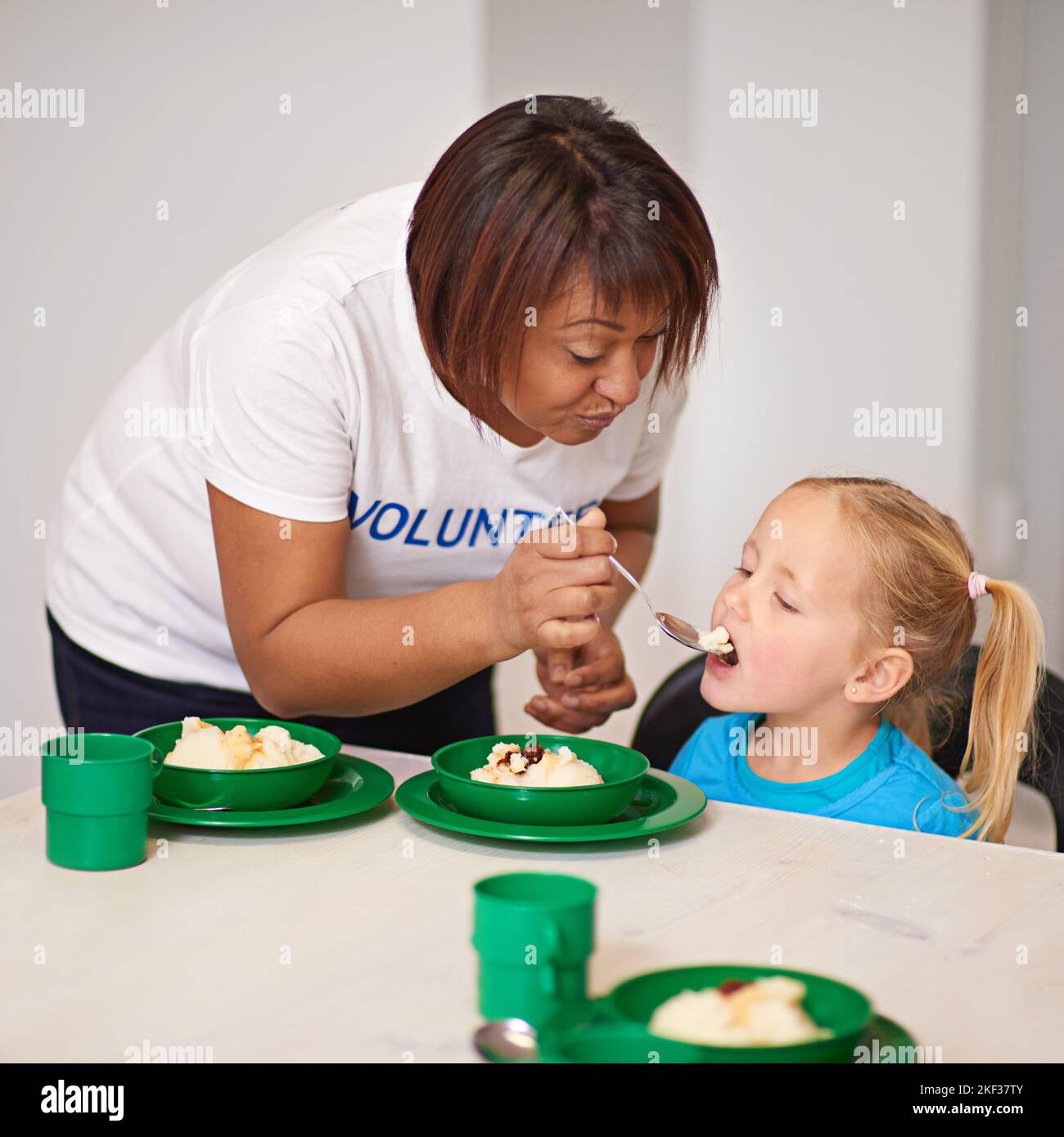 Providing nutritious meals one spoonful at a time. a volunteer feeding a little girl at a youth center. Stock Photo