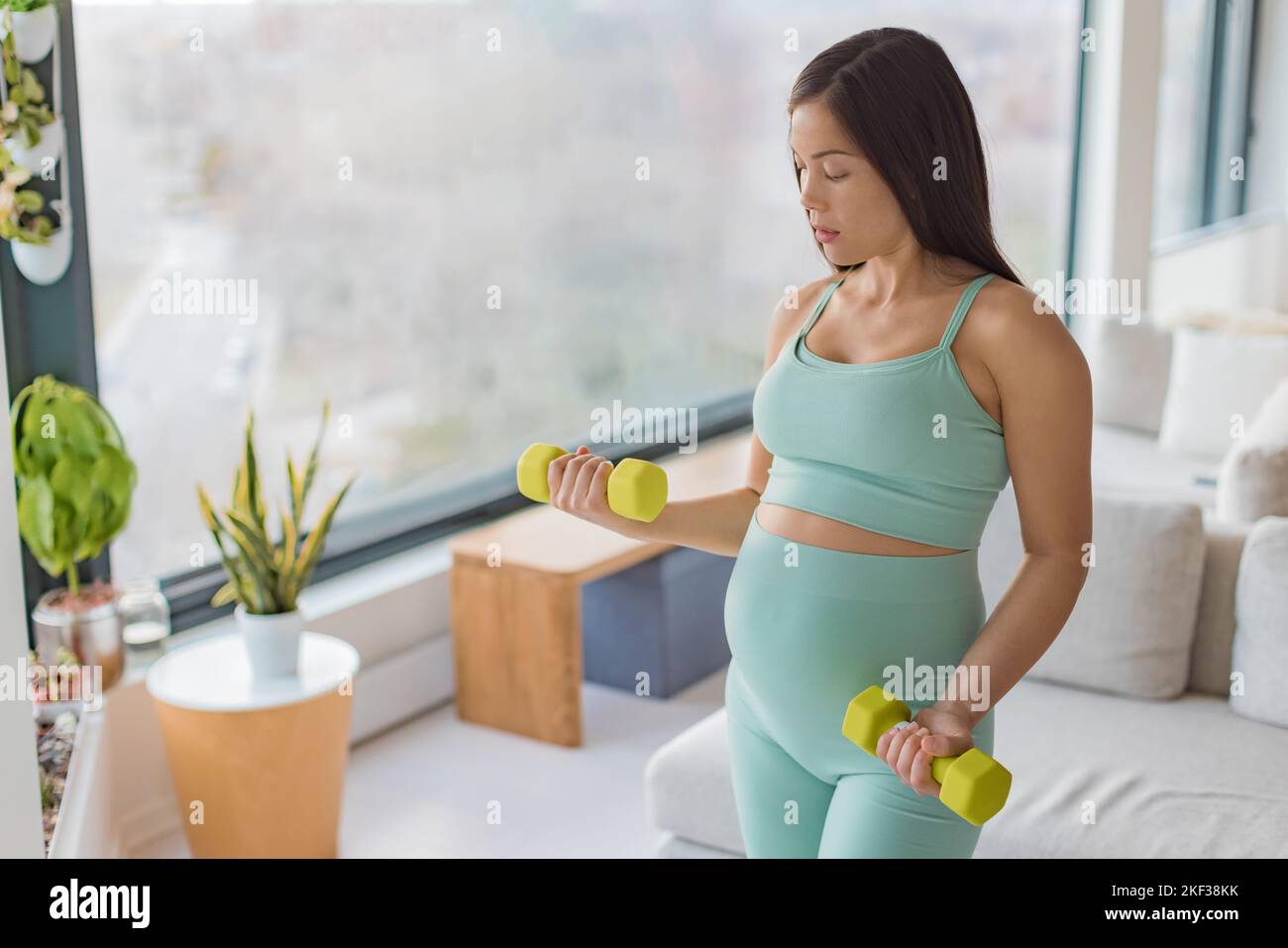 Pregnancy fitness. Pregnant woman home workout fitness strength training exercise with dumbbell weights. Body workout arm curls showing of belly and a Stock Photo