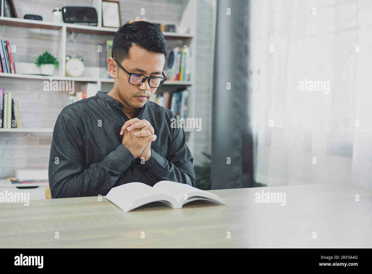 Asian man doing hands together in prayer to God along with the bible In the Christian concept of faith, spirituality and religion, men pray in the Bib Stock Photo