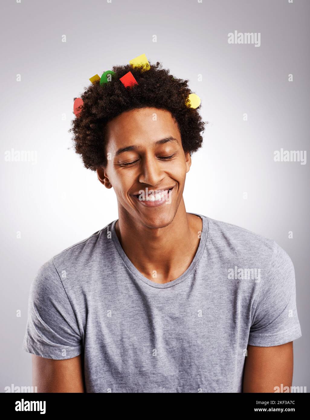 I just love colorful hair...a young man with colorful paper in his hair against a gray background. Stock Photo