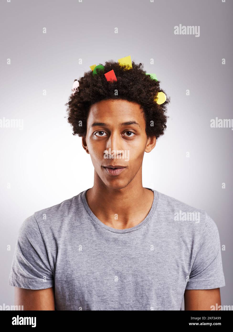 Just go with the fro. a young man with colorful paper in his hair against a gray background. Stock Photo
