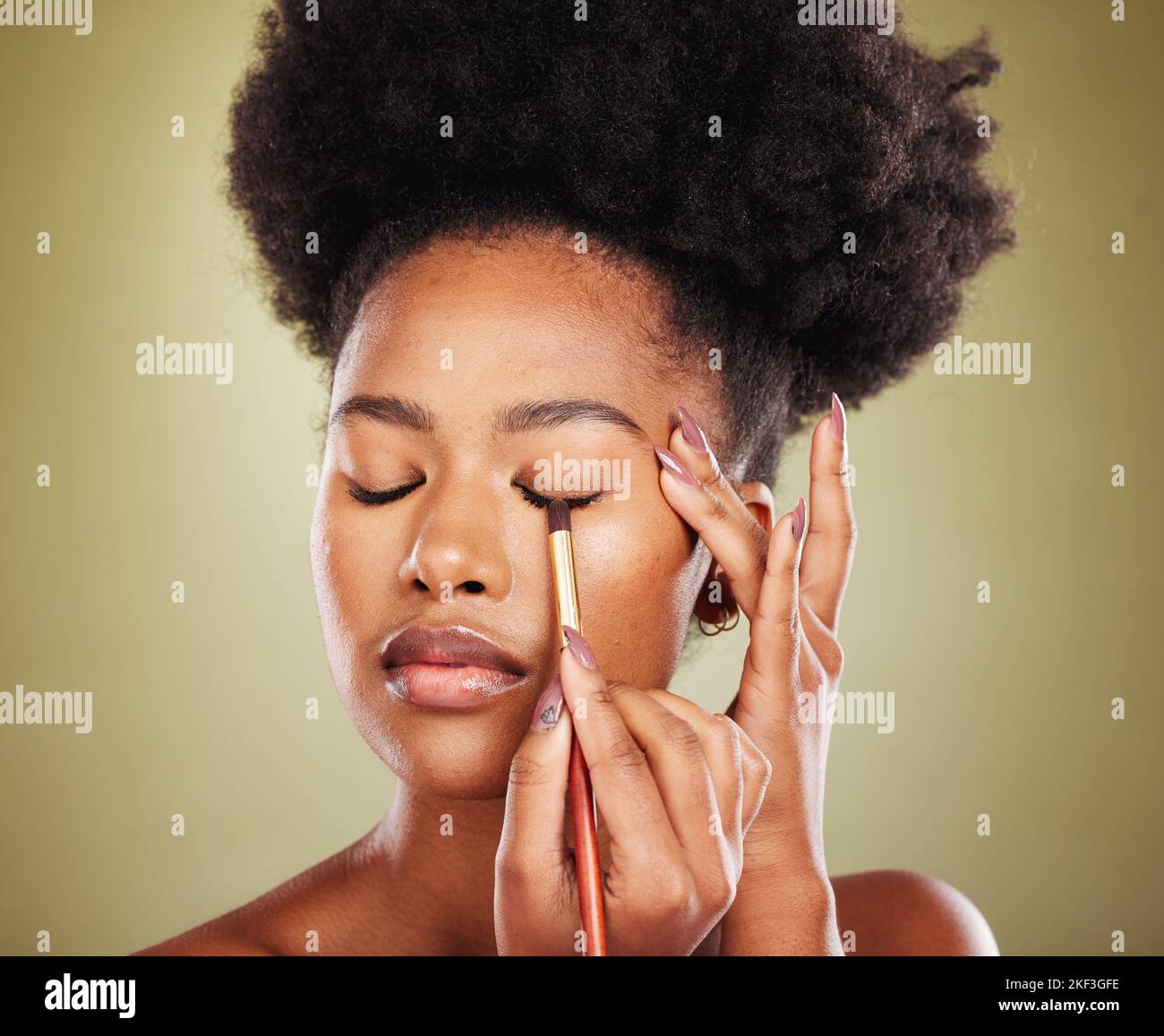 Black woman, eyeshadow makeup and brush in studio on green background. Skincare, self care and young female model holding makeup brush, cosmetics or Stock Photo