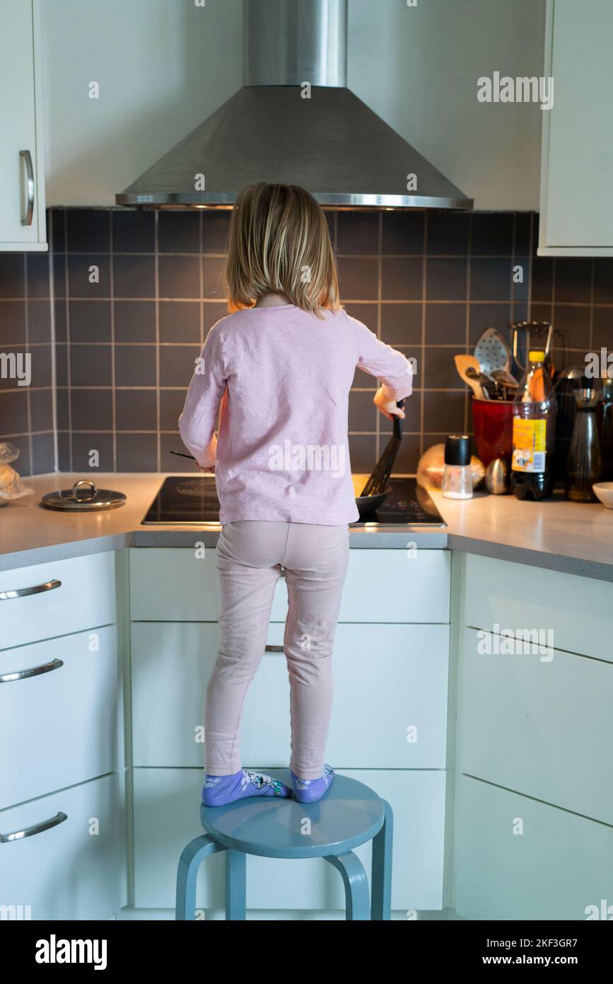 Girl standing on stool while cooking Stock Photo Alamy