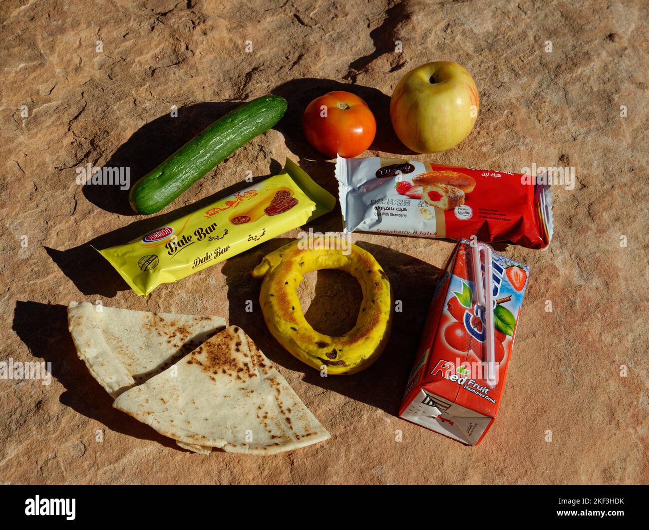Breakfast foods from Jordan. Drink carton, sweet foods, cake in packets, apple, tomato, flatbread, and a small cucumber. Stock Photo