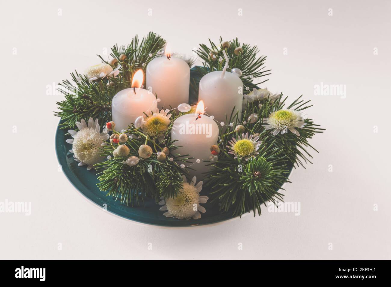 4 white advent candles in religious cristian traditional wreath decorated with green fir and flowers Stock Photo