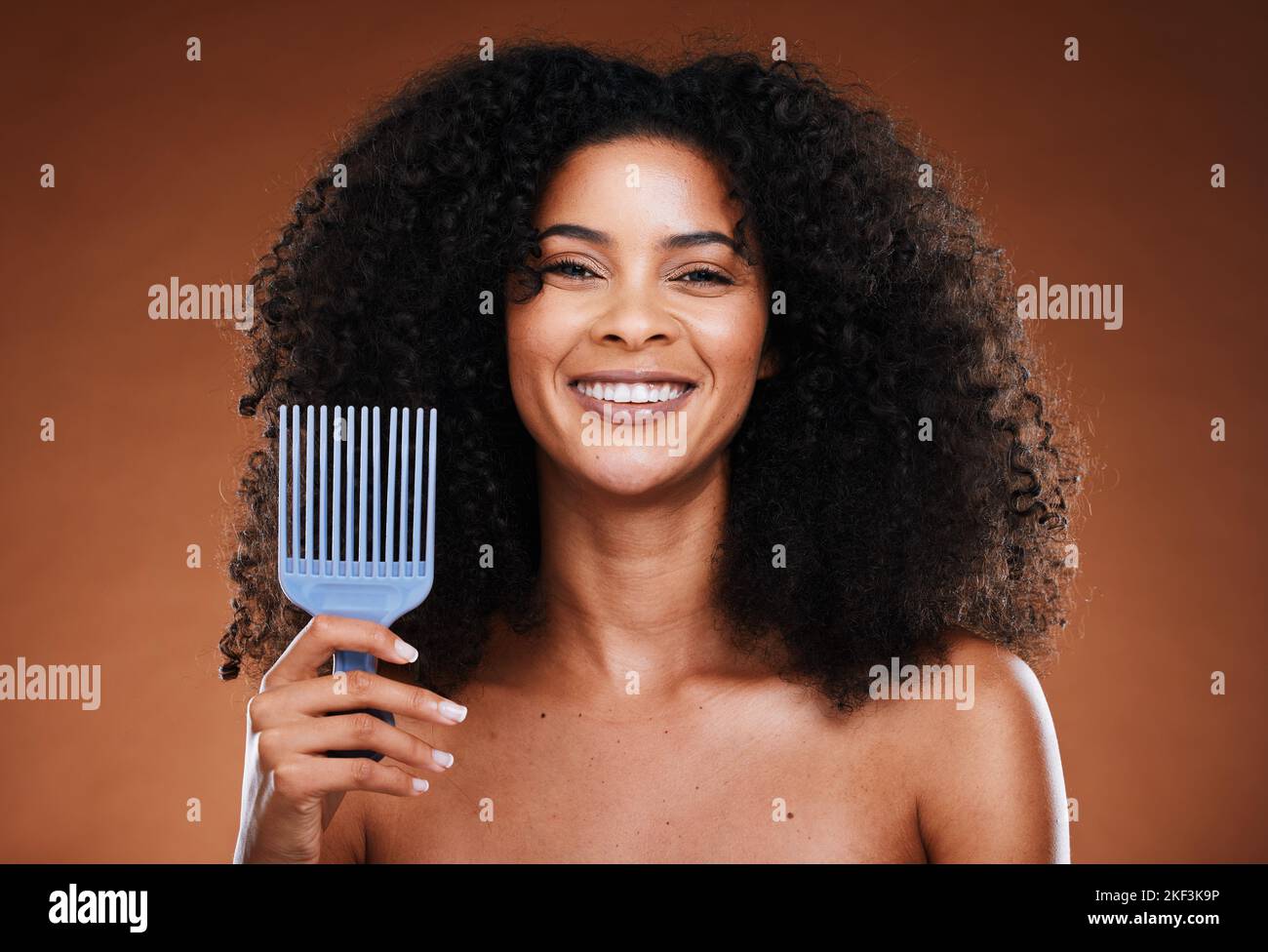 Black woman, hair care and smile in portrait with comb, afro pick or beauty against brown backdrop. Happy African, model and woman with cosmetics Stock Photo