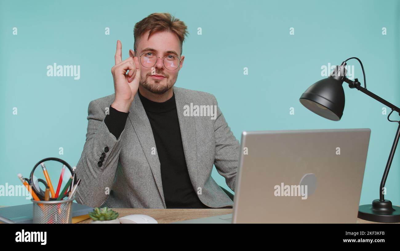 Eureka. Inspired business man sitting at office desk pointing finger up with open mouth, having good idea, plan, startup, showing inspiration motivation gesture, problem solution on blue background Stock Photo