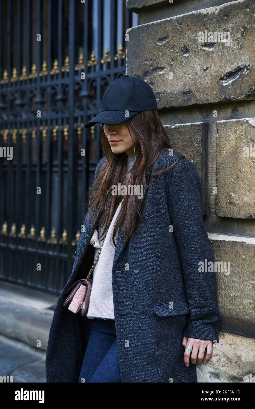 Woman in hat and coat leaning on wall Stock Photo