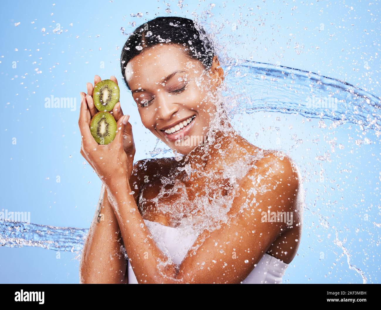 Water splash, kiwi and skincare of woman in studio isolated on a blue ...