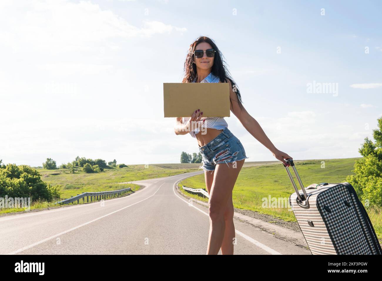 Your text here. Travel and hitch-hiking concept. portrait of happy pretty young woman standing with empty blank. A woman on the road waiting for passi Stock Photo