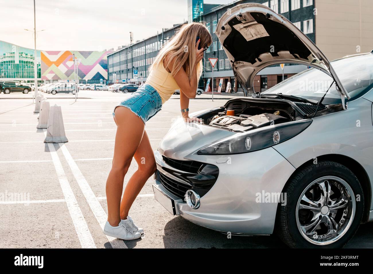 The woman stood near the car that was broken on the road while traveling. open the hood of the gray car. Stock Photo