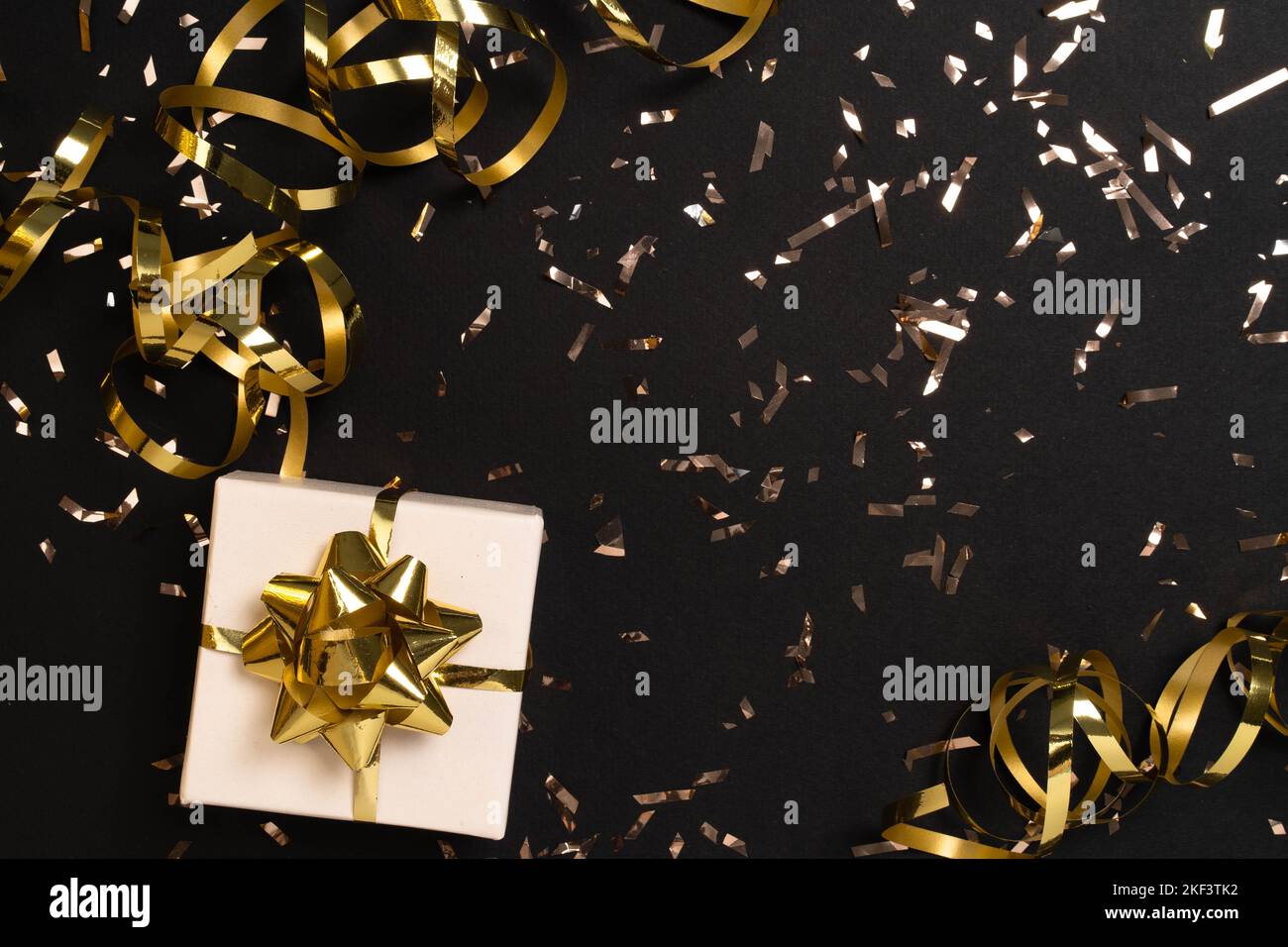 Gift or present box and gold confetti on black table top view. Flat lay composition with copyspace for christmas, new year , birthday, mother day, black friday , sale, promotions, xmas, or wedding.  Stock Photo
