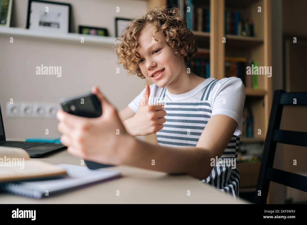 Smiling preteen girl holding and using mobile phone showing thumb up ...