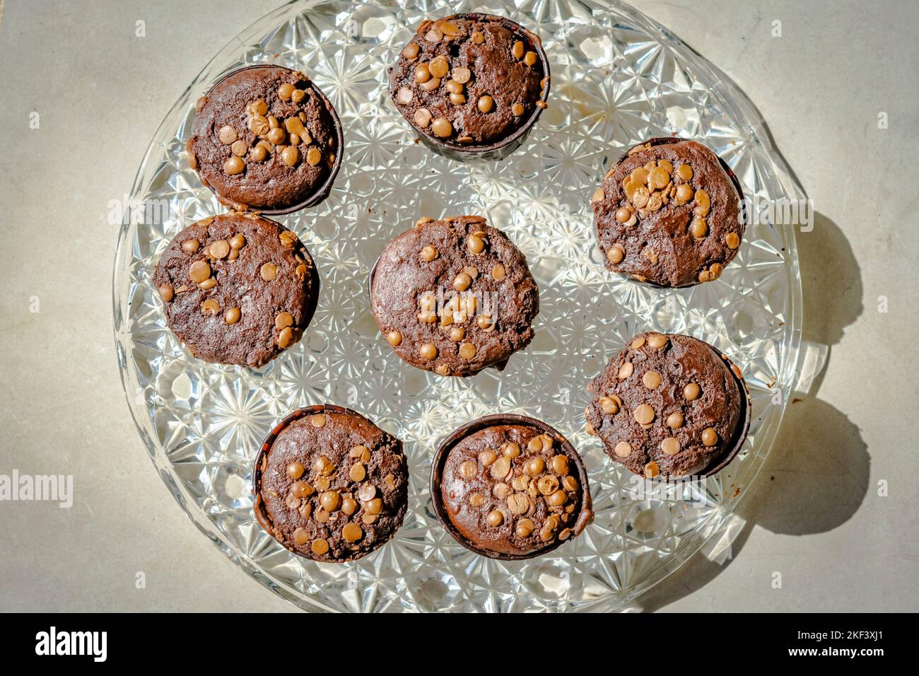 Overhead view of homemade muffins with chocolate chips cakes on a glass plate. Directly above close-up macrophotography with side sunlight shining. Stock Photo