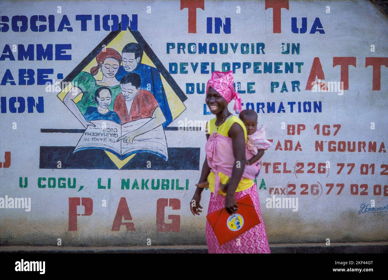 Burkina Faso, Fada N'Gourma. A mother with her child in front of a mural of Tin Tua, an organisation on rural development. Stock Photo