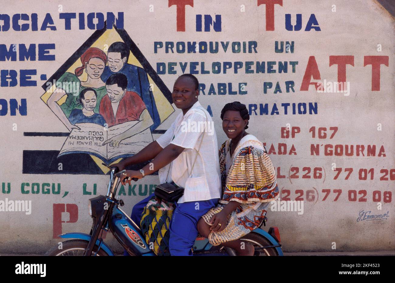 Burkina Faso, Fada N'Gourma. Two young women on a moped in front of a mural of Tin Tua, an organisation on rural development. Stock Photo
