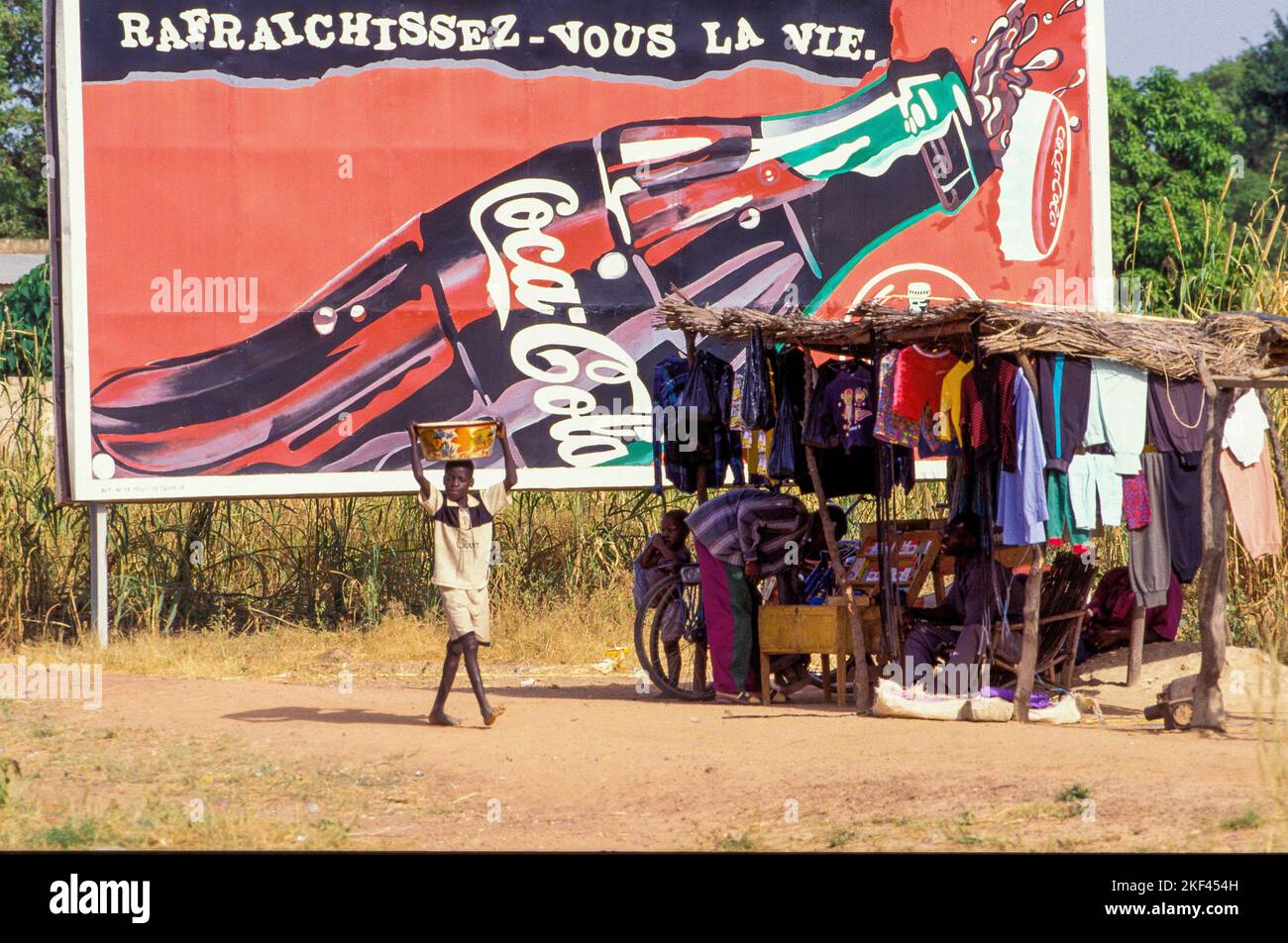 Burkina Faso. A market stall with clothes in front of a Coca Cola billboard. Stock Photo
