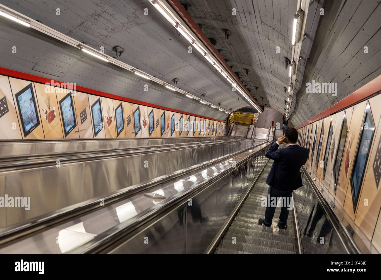 Single man descending escalator into subway while talking on phone Stock Photo