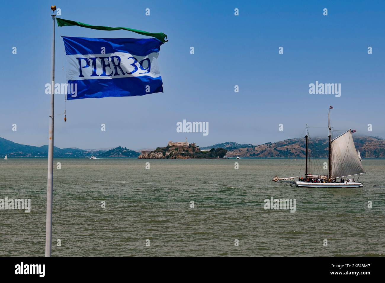 Fahne von Pier 39 und historisches Segelboot in der San Francisco Bay, hinten die Insel Alcatraz, San Francisco, Kalifornien, USA, Nordamerika Stock Photo