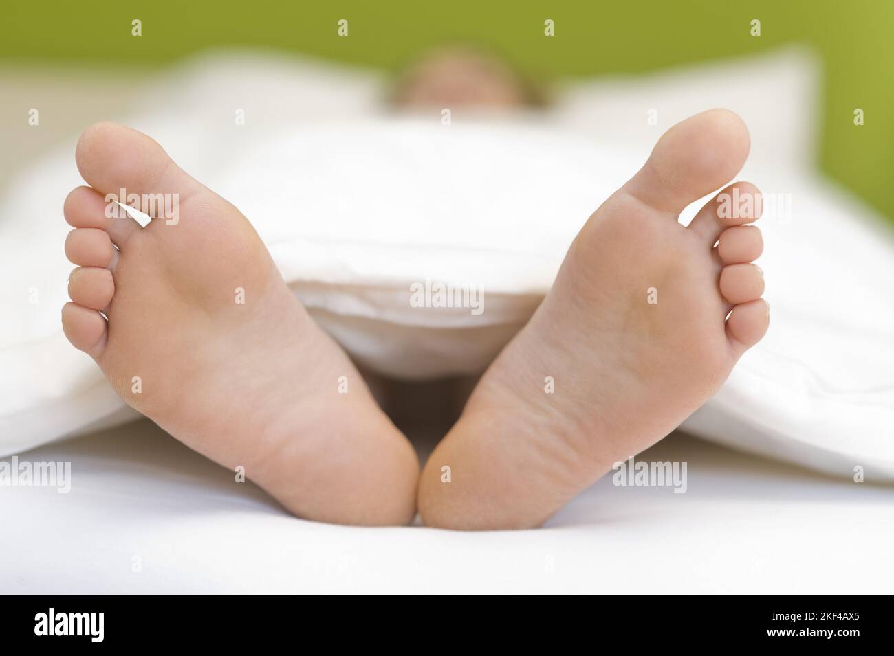 Zwei Füsse schauen unter der Bettdecke hervor Stock Photo