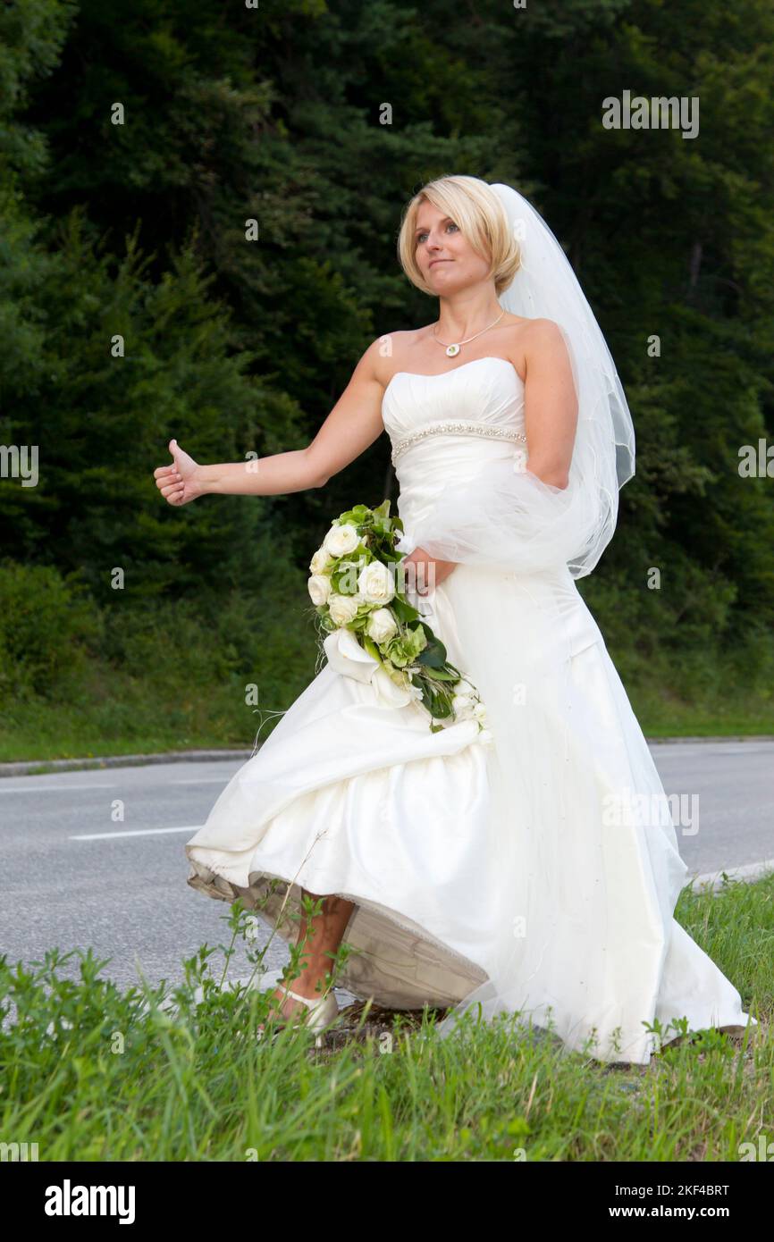 Eine fröhliche Braut steht an der Strasse per Anhalter, Hochzeitsspaß, Hochzeitspass, Tradition, Entführung der Braut, Stock Photo