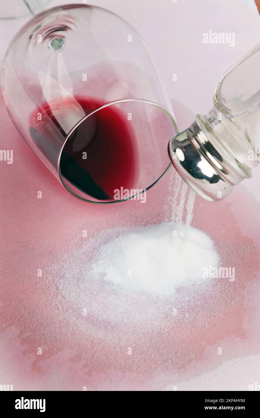 Ein umgestürztes Glas Rotwein hinterlässt einen grossen Rotweinfleck auf einer Tischdecke. Reinigen und entfernen mit Salz als Reinigungsmittel, Stock Photo