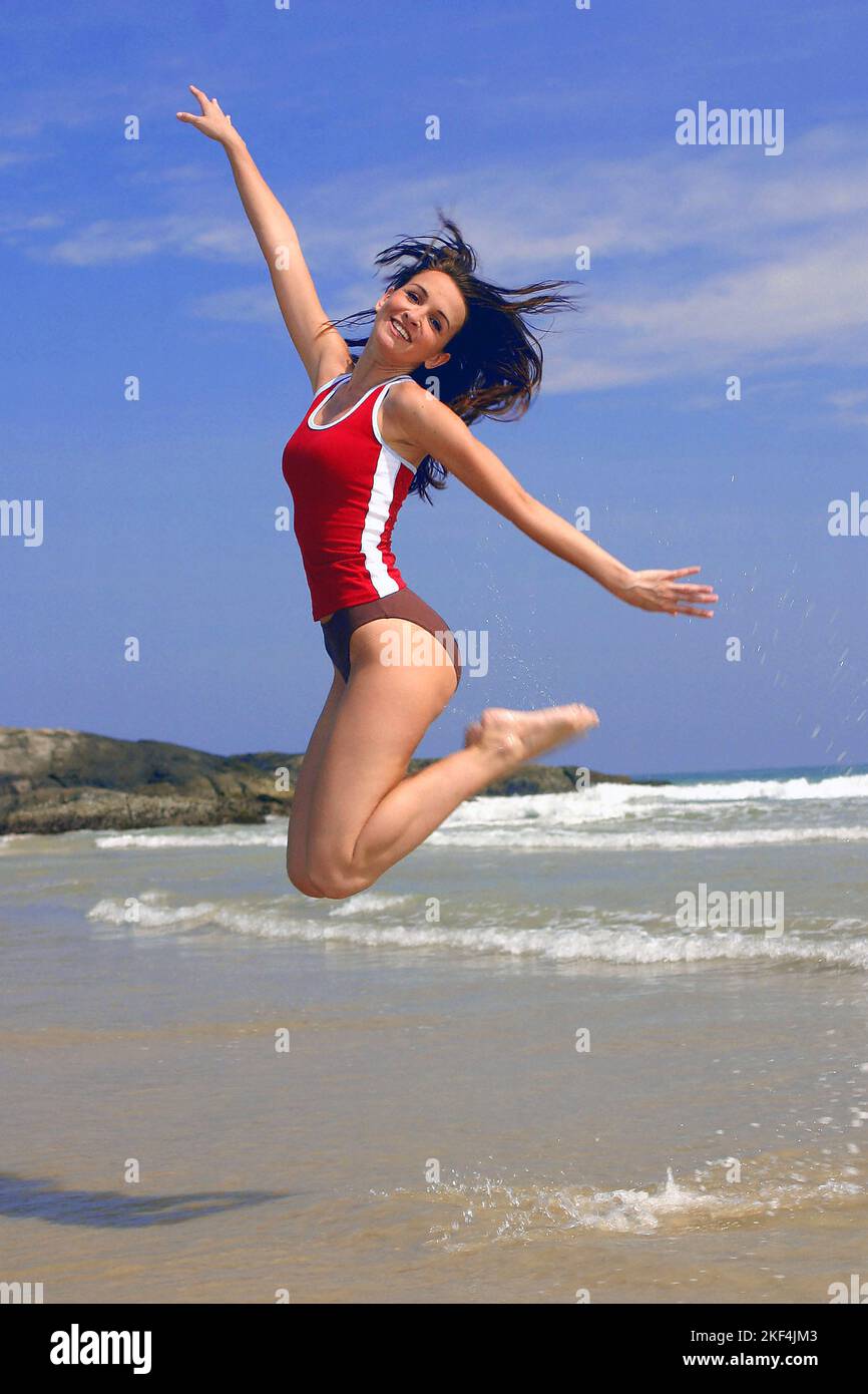 Eine junge Frau springt vor Freude in die Luft, 25, 30, Jahre, dunkelhaarig, Shirt, Bikini, Strand, Urlaub, Urlaubsfreuden, Stock Photo