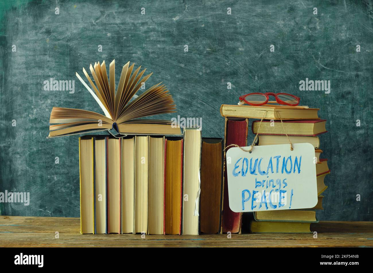 Stack of hardback books with Education brings peace slogan sign blackboard background.Learning,education,global thread,reading,schooling concept. Free Stock Photo