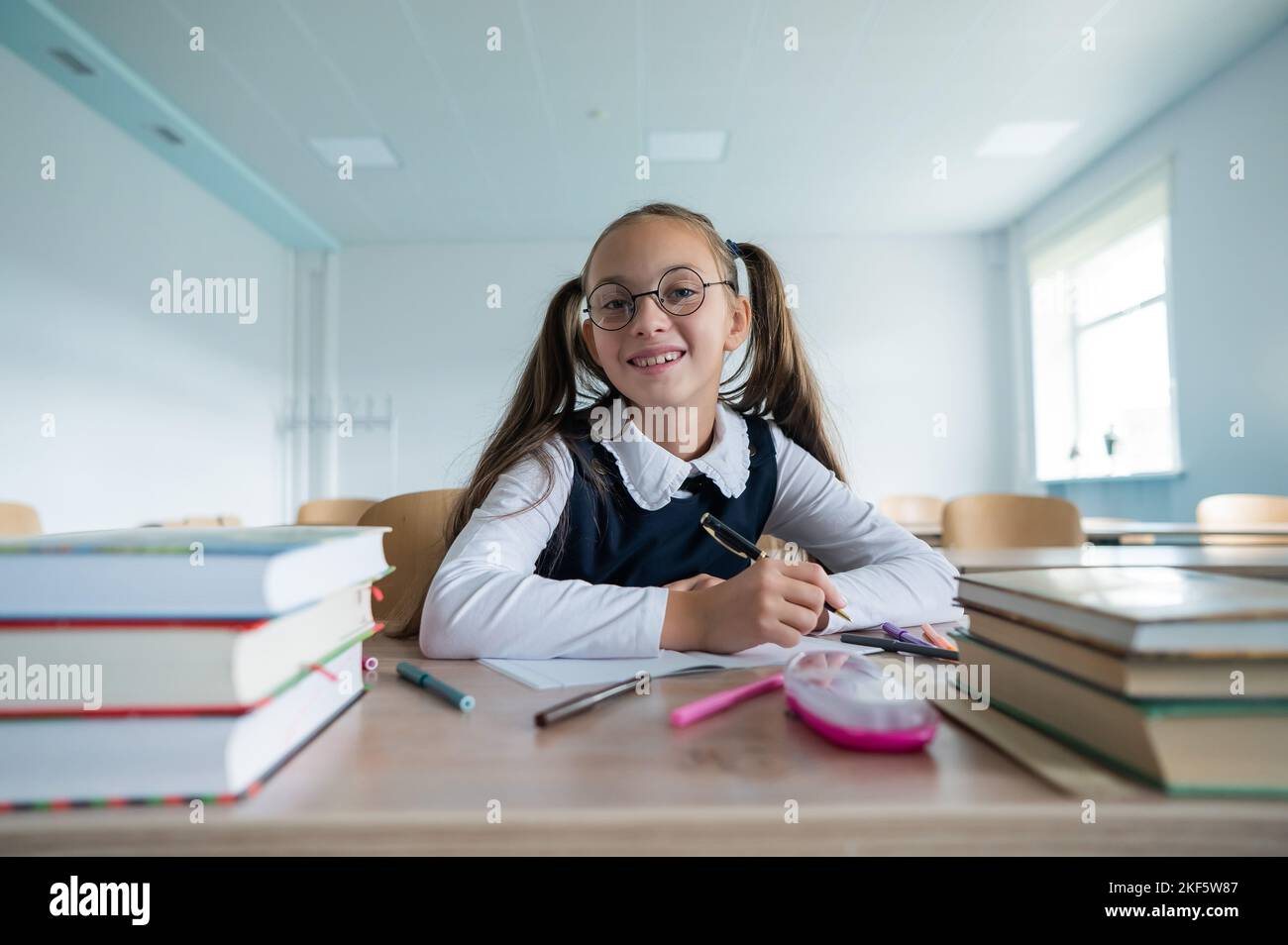 Caucasian girl with two ponytails sits at her desk and writes in a workbook. Stock Photo