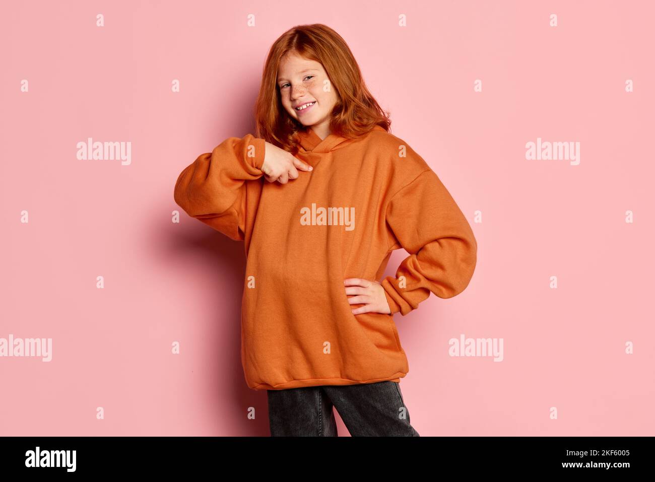 Smiling teen girl, emotional kid with long red hair and freckles posing isolated over pink background. Concept of children emotions, casual sports Stock Photo