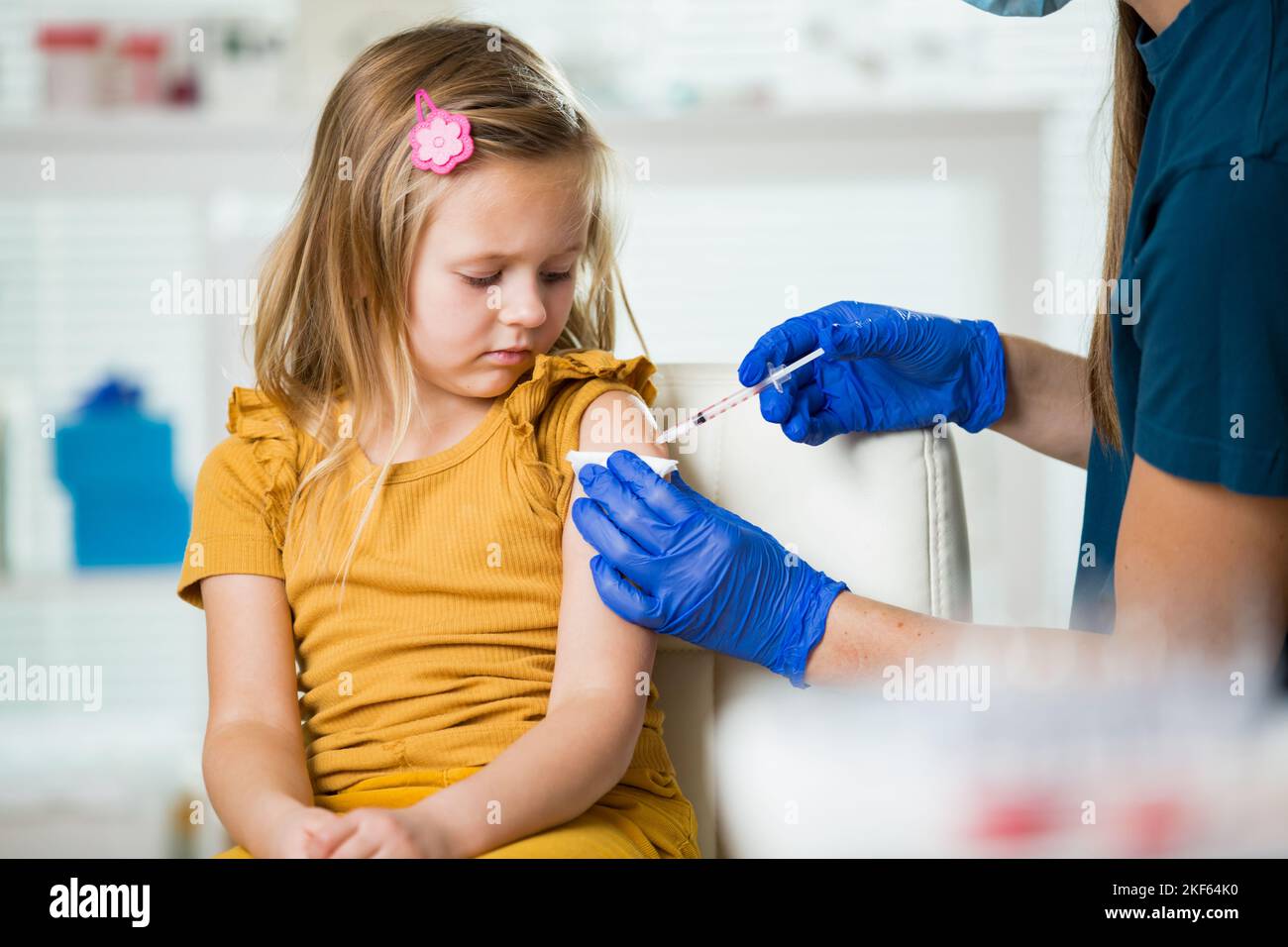 Female nurse with surgical mask and in gloves giving vaccine injection to a child in clinic. Children vaccination. Stock Photo